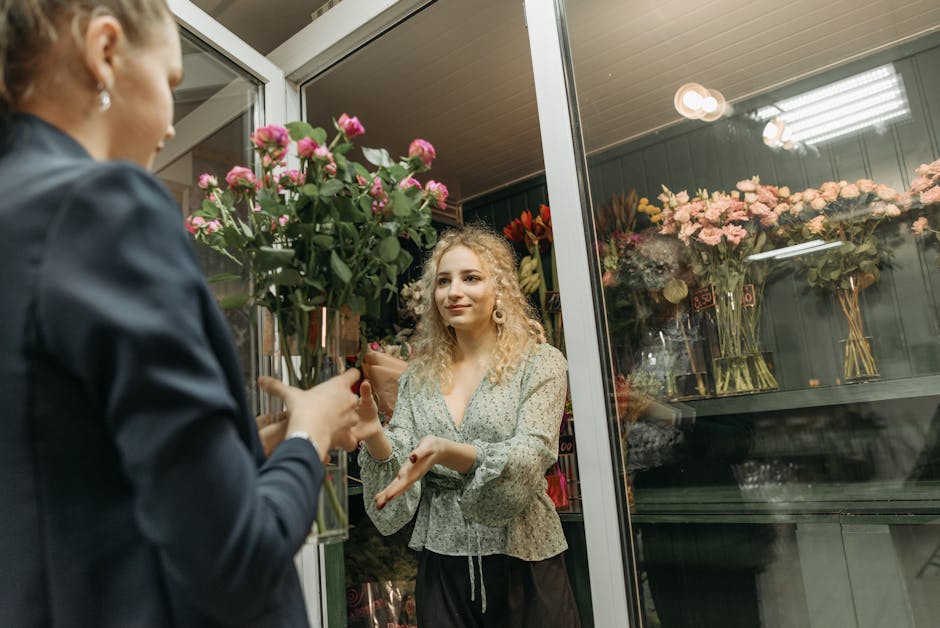 A customer at Putney Florist, part of putneyflorist.org.uk, is pictured inside a flower shop exchanging a vibrant bouquet of pink roses with a staff member. The roses, arranged neatly with lush green